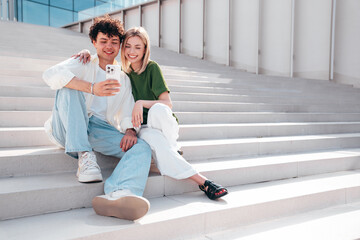 Smiling beautiful woman and her handsome boyfriend. Couple in casual summer clothes. Happy cheerful family. Female and man having fun. They posing in the street in sunny day. Sit at stairs