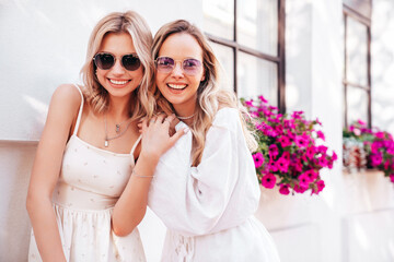 Two young beautiful smiling cute women in trendy summer sundress. Sexy carefree models posing in the street in sunny day. Positive models having fun and hugging. Cheerful and happy, Europe, Santorini