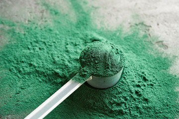 Green spirulina powder in a plastic measuring cup - healthy nutritional supplement