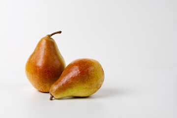 Two ripe, yellow pears lie on a white surface, one slightly overlapping the other. The pears have a glossy surface and a slightly reddish hue