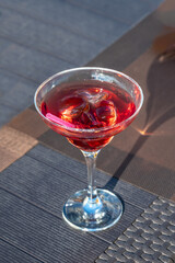 Vermouth cocktail with ice in the vermouth glass on the table under sun light.