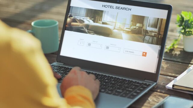 back view of man at computer doing hotel room research on the web,male at the laptop planning vacation searching for hotels accommodation online on the internet website