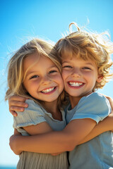 Two young children hugging each other tightly on a sunny day, their bright smiles showcasing sibling love and joy, with a clear blue sky in the background.