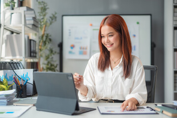 Young asian businesswoman smiling and working with digital tablet while analyzing business data at modern office