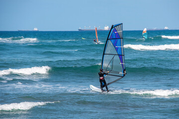 Windsurfer gliding across azure waves under clear sky with distant ships at sea