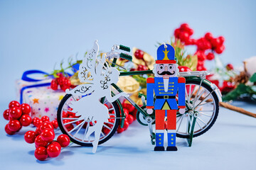 fairytale picture with toy bicycle, New Year fairy, toy nutcracker, against the background of Christmas attributes and blue background, postcard, congratulations, creative trick