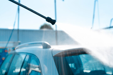 Water streams over  car while being sprayed at bright, sunny outdoor car wash