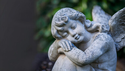 Fototapeta premium Gray stone sculpture of sleeping guardian angel. Antique statue with closed eyes. Religion concept