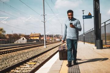 Happy man with a suitcase using phone while walking on the railway station.	