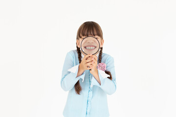 Happy little schoolgirl in uniform with magnifier on white background