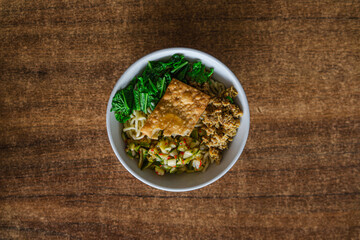 mie ayam or chicken noodle served on a white ceramic bowl and with a wooden background, looks very delicious.