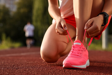 Woman tying shoelace of pink sneaker at stadium, closeup. Space for text
