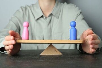 Gender equality concept. Woman with male and female figures on scales at dark table, closeup