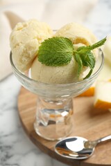 Scoops of melon sorbet with mint in glass dessert bowl, fresh fruit and spoon on light marble table, closeup