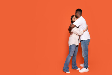 Couple Embracing in Warm Hug Against Vibrant Orange Backdrop Indoors