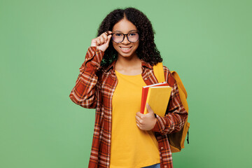 Young smart happy teen girl student wear brown yellow casual clothes backpack bag hold books touch glasses look camera isolated on plain green color background. High school university college concept.