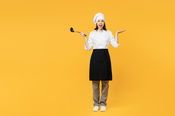 Full body young chef cook baker woman wear white shirt apron uniform toque chefs hat hold in hand soup black ladle dipper spread hand isolated on plain yellow background studio. Cooking food concept.