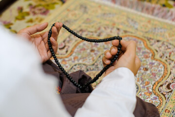 Close up Rear view shot of a hand man holding prayer beads, set against a colorful, patterned...