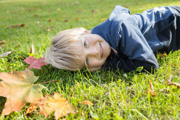 child lies on the grass strewn with autumn leaves on a warm autumn day. joy, positive atmosphere, happy carefree childhood. Active lifestyle, Indian summer. Hello autumn