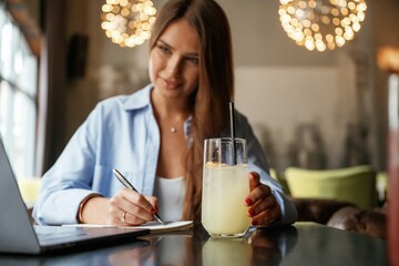 Cocktail is on the table. Beautiful woman with laptop is in the bar