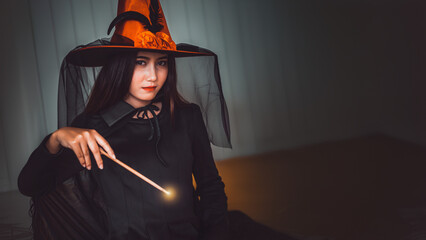 Attractive beautiful Asian woman dressed as a witch using magic wand casting spell, Halloween...