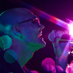 Neon hues reflect off singer's face as he belt out powerful note, creating striking image of...