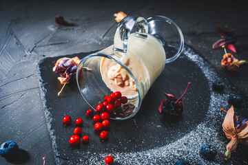Panna cotta in a transparent glass lying on a black mica board with lingonberries, blueberries and...