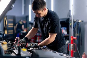 Obraz premium in a car service a master in a black T-shirt uses a drill to unscrew the bolts in the engine part of the car replacing spare parts