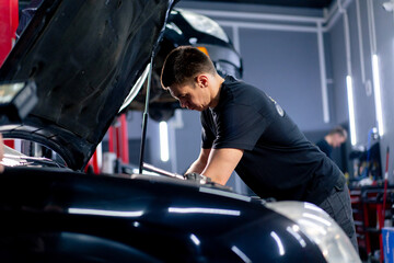 Naklejka premium in a car service a master in a black T-shirt uses a drill to unscrew the bolts in the engine part of the car replacing spare parts