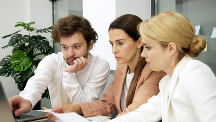 Business team in a modern office using a laptop for financial analysis. They brainstorm and discuss a corporate project, collaborating on solutions. Perfect for teamwork and financial strategy themes.