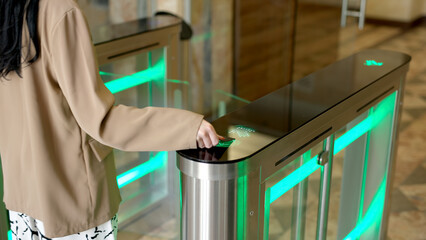 A confident businesswoman effortlessly passes through a modern turnstile using her personal access card in a sleek office lobby. Ideal for concepts of advanced security, workplace technology.