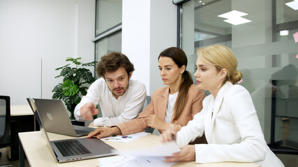 Business team in a modern office using a laptop for financial analysis. They brainstorm and discuss a corporate project, collaborating on solutions. Perfect for teamwork and financial strategy themes.