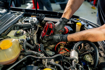 Obraz premium close up in a car service a master in a black T-shirt uses a drill to unscrew the bolts in the engine part of the car replacing spare parts