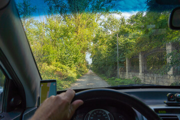 View from the windshield of a car onto a shady dirt road between green trees