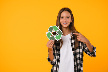 Smiling caucasian eco-activist student schoolgirl pupil pointing at recycling logo sign for environment protection, sorting garbage isolated in yellow background