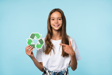 Happy caucasian eco-activist student schoolgirl pupil pointing at recycling logo sign for environment protection, sorting garbage isolated in blue background