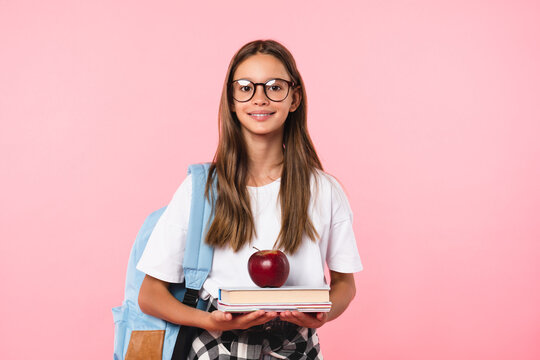 Best student pupil teenage girl with excellent marks going back to school with books and apple isolated in pink background. New academic educational year begins starts.