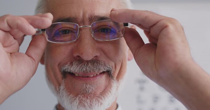 Close up portrait of a happy Caucasian senior man is wearing eyeglasses, with an eye chart in the background, in clinic. Vision and optic wear, showcasing his businessman like appearance.