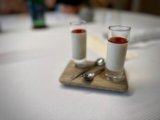 Elegant Presentation of Creamy Dessert Shooters with a Red Sauce Layer Served on a Wooden Board with Silver Spoons in a Fine Dining Setting