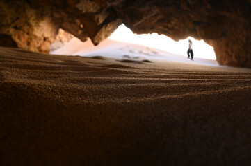 Young woman hiking in the background of a red natural rock cave in Algarve Portugal by the atlantic...