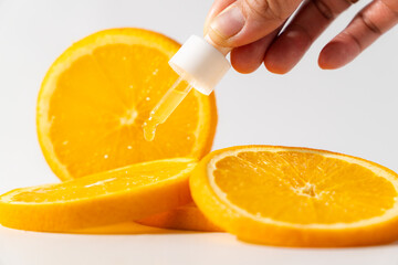 Woman's hand and brown amber glass bottle of face serum or oil, with pile of orange slices in the...
