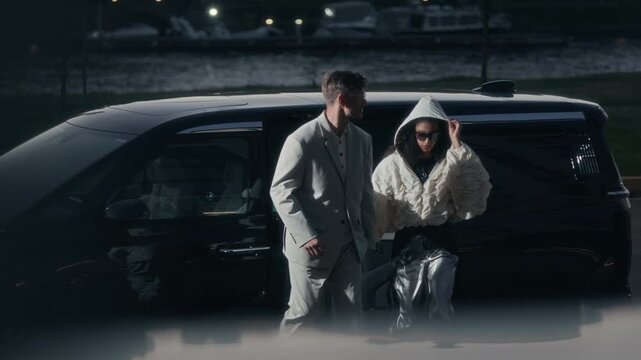 Paparazzi shot of interracial celebrity couple getting out of black car with tinted windows in street. Biracial diva hiding her face under dark sunglasses and hood