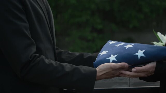 Close up shot of unrecognisable man passing American flag folded in triangle to woman at outdoor memorial ceremony
