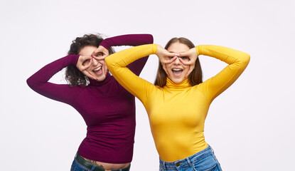 Two cheerful women in colorful outfits posing playfully with hands on their faces, expressing joy and friendship.