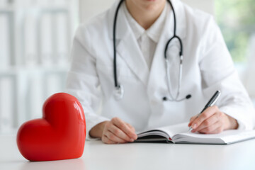 Doctor working at table in clinic, focus on red heart