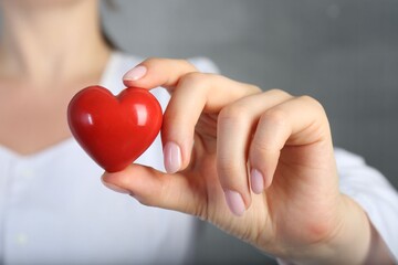 Doctor holding red heart on grey background, closeup