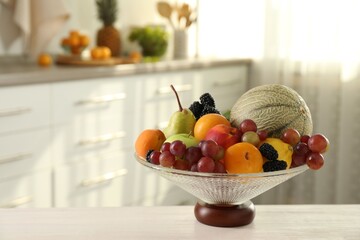 Glass vase with different fruits and berries on white table indoors