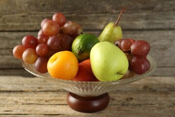 Glass vase with different fresh fruits on wooden table, closeup