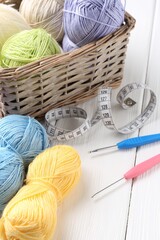 Crochet hooks, measuring tape and colorful yarns on white wooden table, closeup