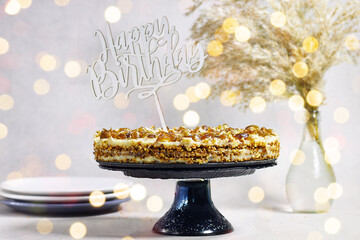 Homemade Russian Honey dates and peanuts cake in stand cake with reed vase . Honey cake Medovik with happy birthday text and bokeh